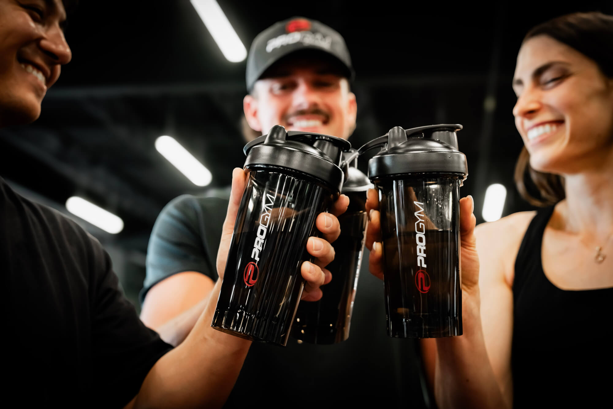 Trois personnes trinquant avec des shakers ProGym noirs à la salle de sport