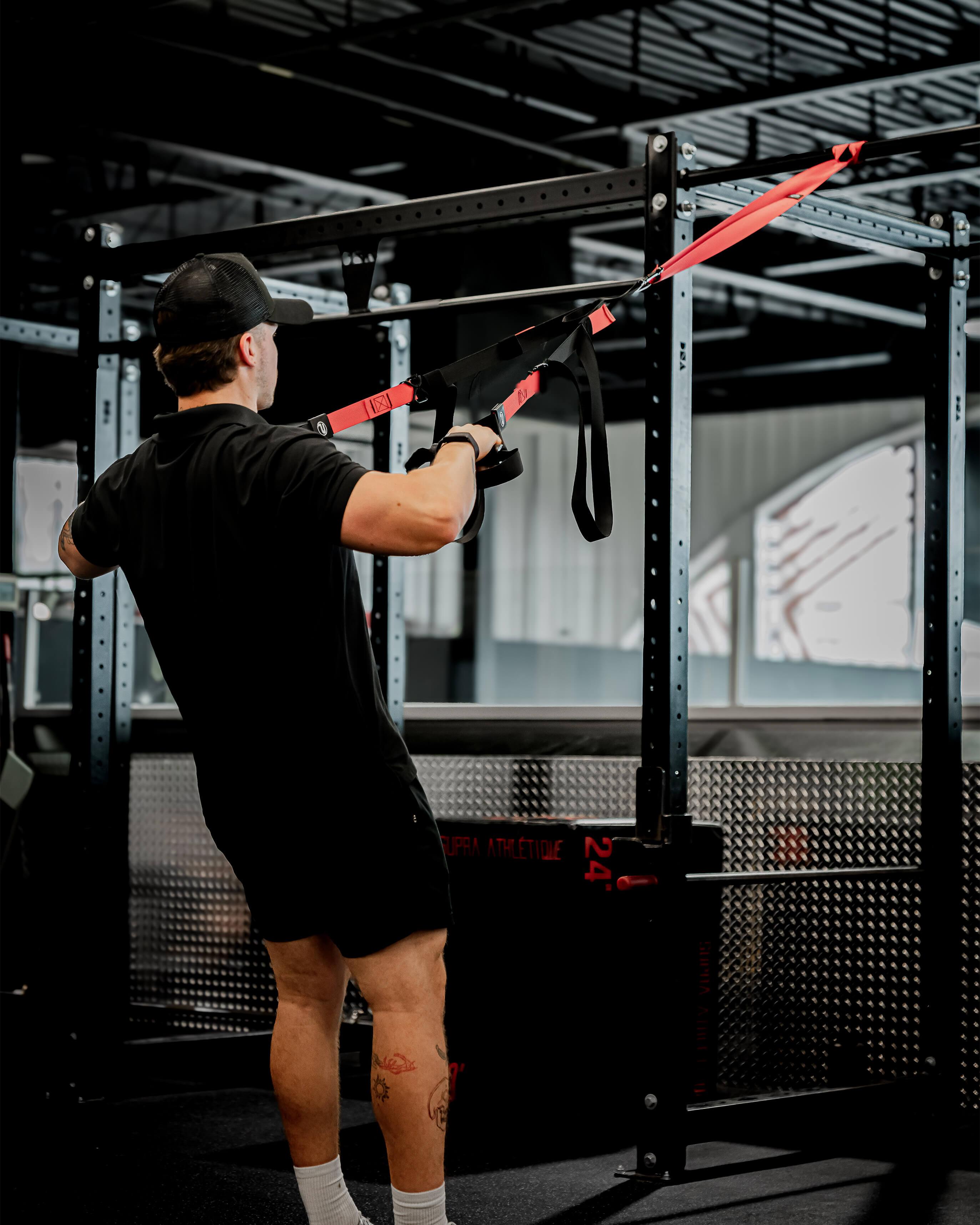 Athlète utilisant les sangles d’entraînement en suspension TRX ProGym rouge et noir à la salle de sport